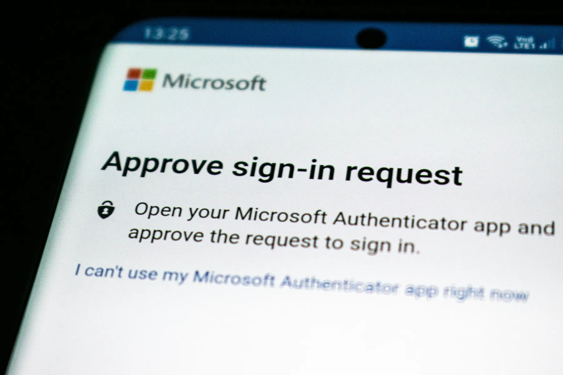 Business owner using a smartphone and laptop for multi-factor authentication at an office desk